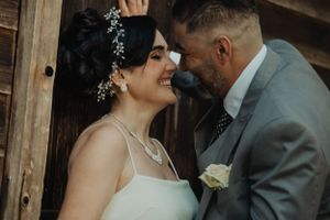 A romantic wedding moment captured as a couple shares an intimate laugh against a rustic wooden backdrop.