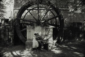 A vintage black and white photo showing a large water wheel structure in a garden setting.