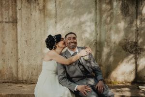 A candid wedding photo showing a joyful moment against a textured wall in natural lighting.