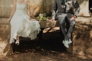 Wedding couple sitting on stone steps with white dress and grey suit details visible.
