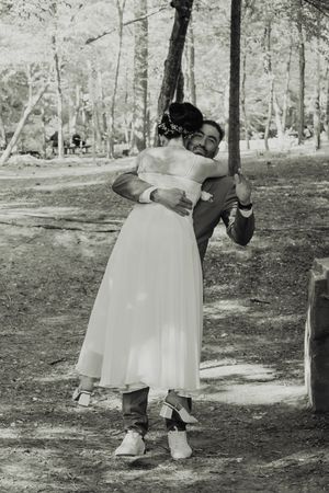 A black and white photo of a romantic embrace in a wooded setting.