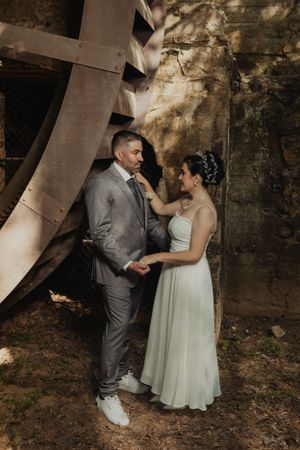 Wedding portrait under an industrial wheel structure with dramatic lighting and shadows.