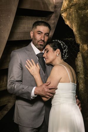 Dramatic wedding portrait with moody lighting showing intimate embrace beneath industrial structure.