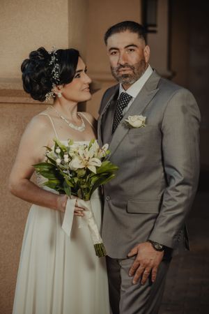 An intimate indoor wedding portrait featuring a white bouquet with orchids.