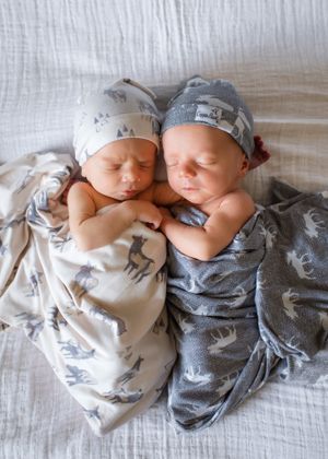 Twin babies sleeping peacefully in matching patterned outfits on white bedding.