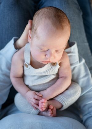 Sleeping infant wearing grey overalls rests peacefully on blue fabric.