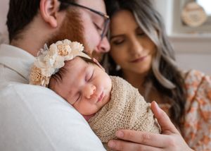 Intimate family moment with sleeping newborn wrapped in knit blanket.