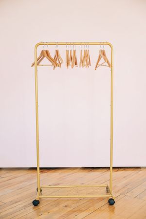 Gold clothing rack with wooden hangers on wheels against white wall.