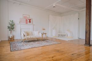 Modern studio space with vintage furniture, area rug, and white curtains against exposed brick walls.