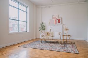 Bright minimalist studio space with white walls, hardwood floors, and a decorative area rug near large windows.