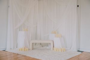 Elegant white drapes frame a minimalist bedroom setup with glowing table lamps and plush carpet.