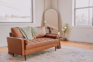 Cognac leather sofa positioned against white walls in a minimalist living room with hardwood flooring.