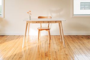 A minimalist wooden table and chair set against white walls in a sunlit room.