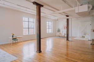 Bright loft studio space with hardwood floors, white walls, exposed columns and large windows.