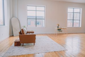Minimalist living room with leather armchair, area rug, and bright windows in a sunlit loft space with hardwood floors.