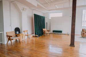 Large empty studio space with hardwood floors, white walls, exposed beams, and green curtains in the background.