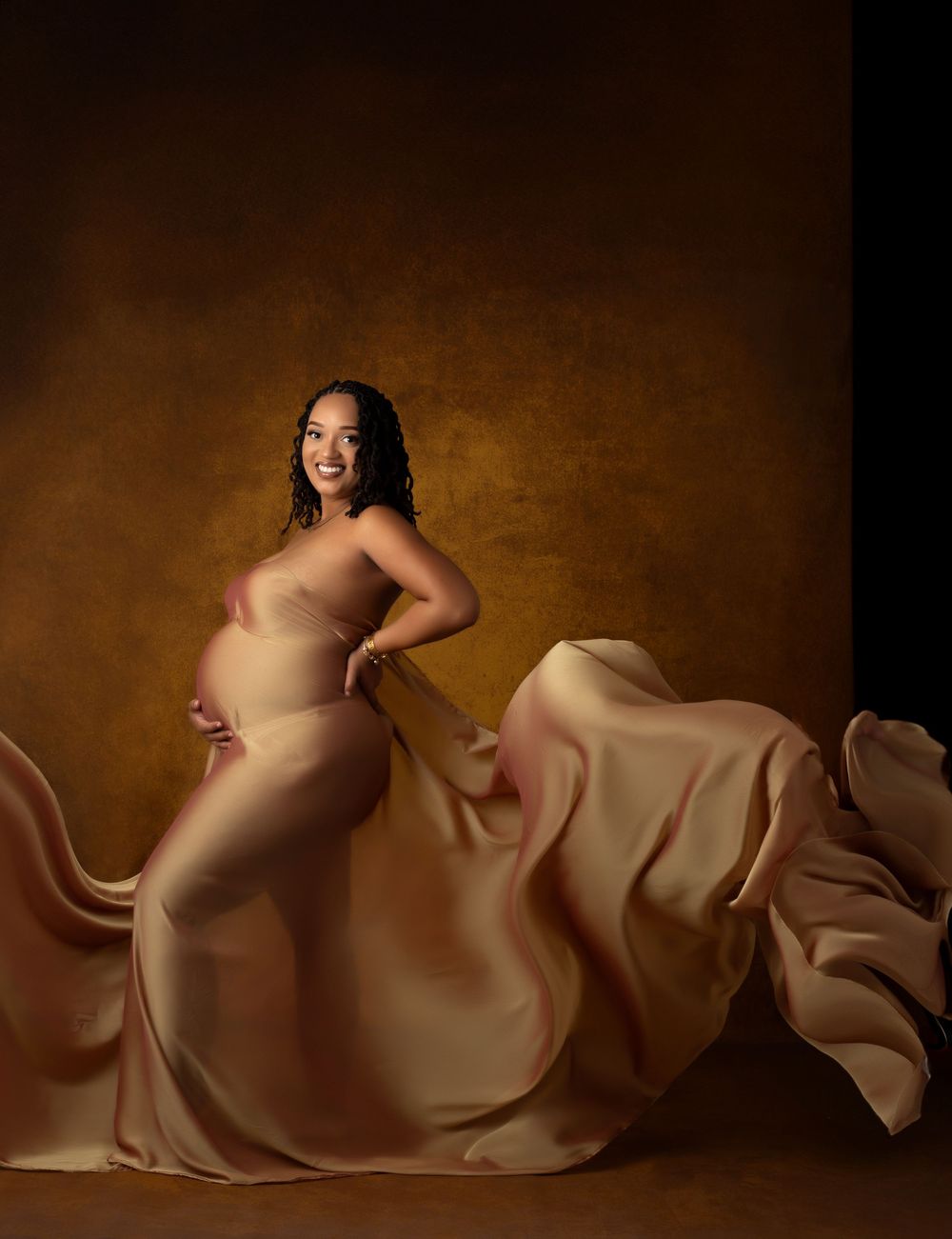 A series of artistic maternity photos showing a pregnant women draped in flowing gold silk fabric against a dark gold textured backdrop.
