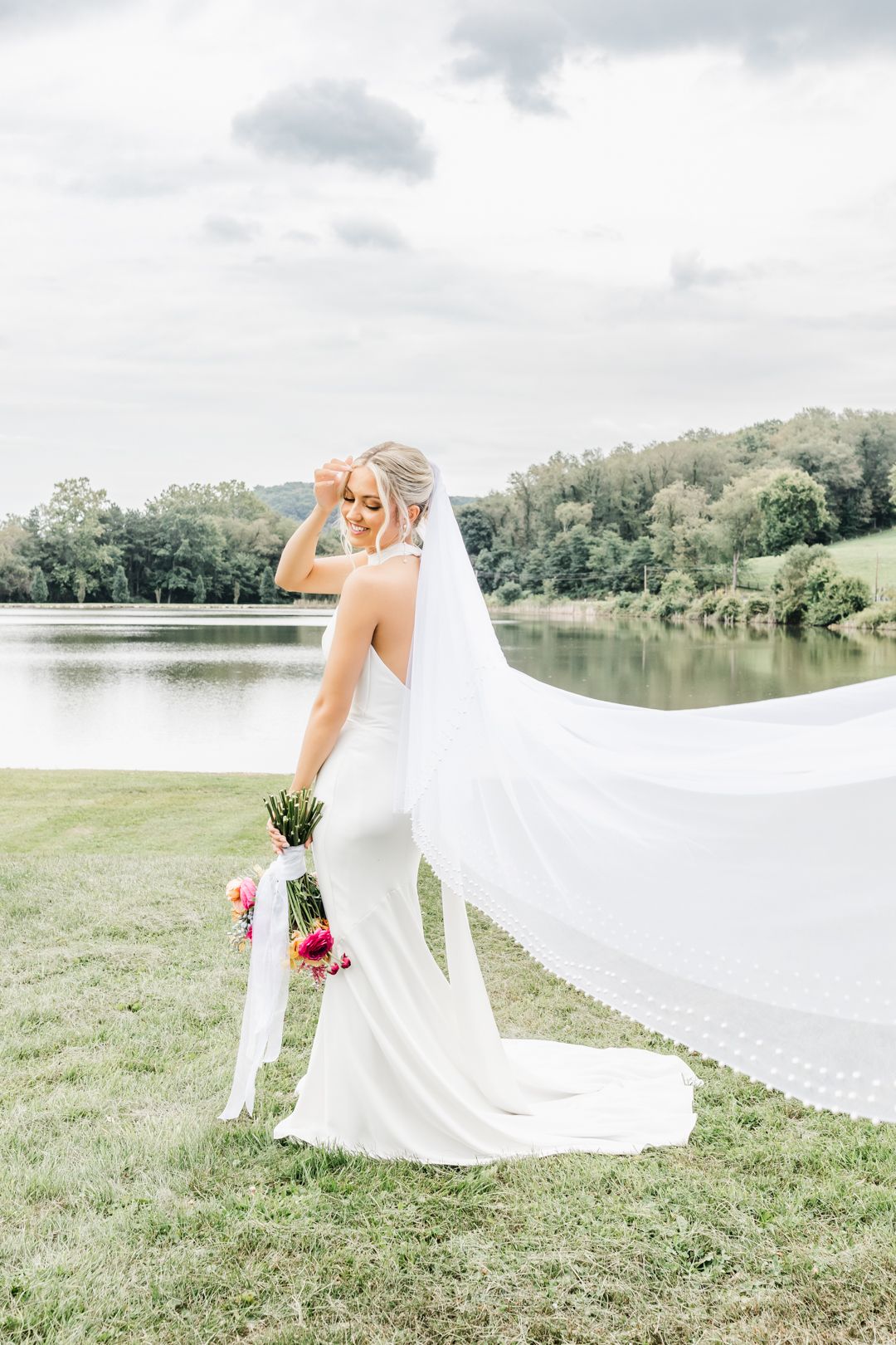 A flowing white wedding dress and veil catch the breeze near a serene lake. Pittsburgh wedding Photographer