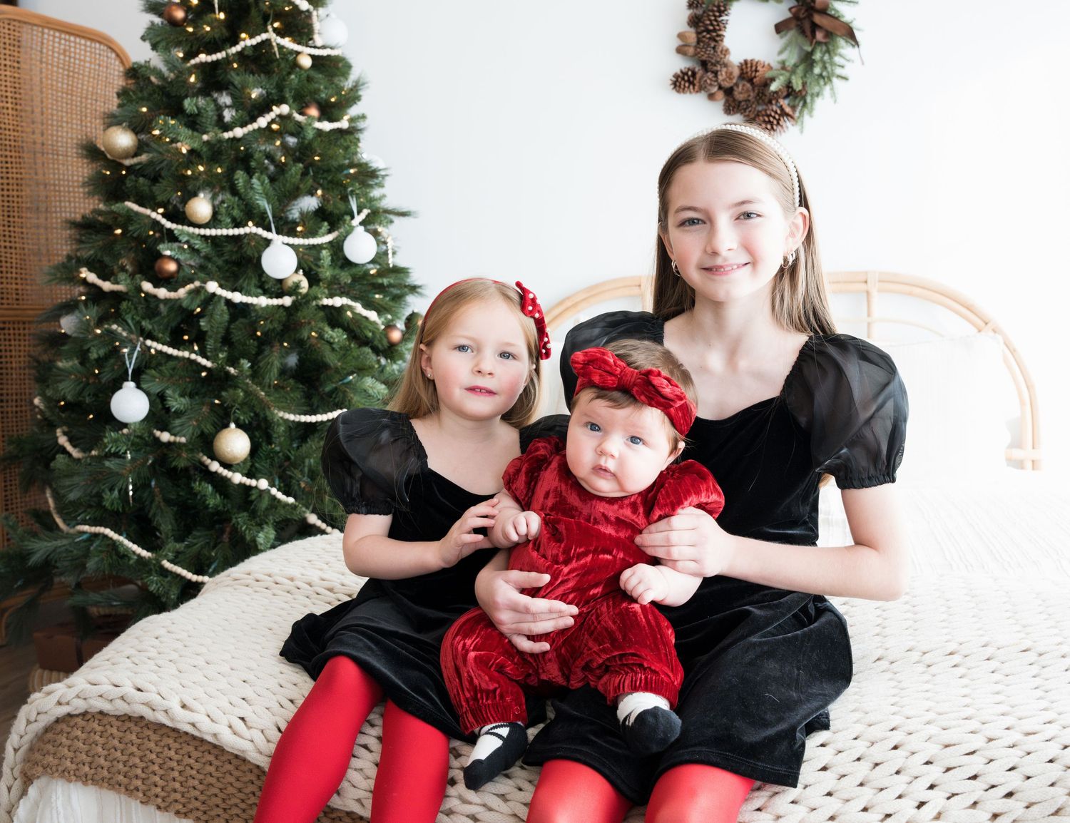 Three people in matching black outfits and red accents pose on white couch by Christmas tree.