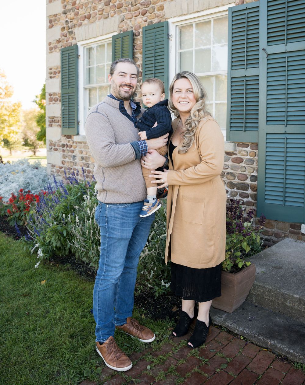 A family poses outside a historic building with green shutters and brick walls.