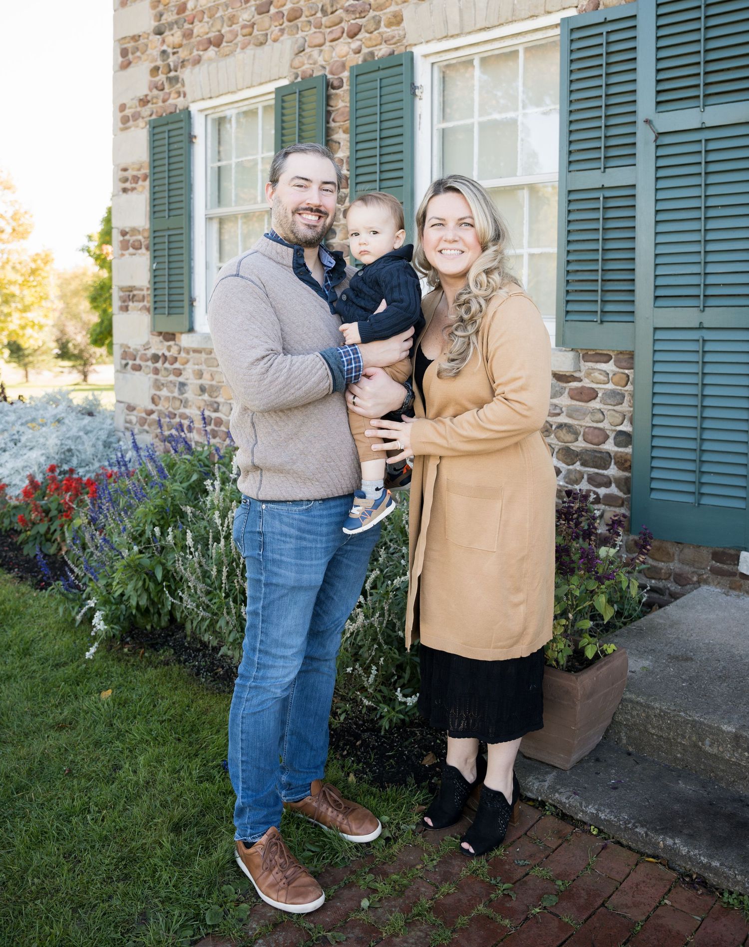 A family poses outside a historic building with green shutters and brick walls.