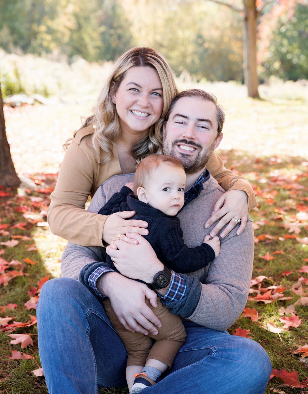 A family sits together on fallen leaves during an autumn photoshoot.