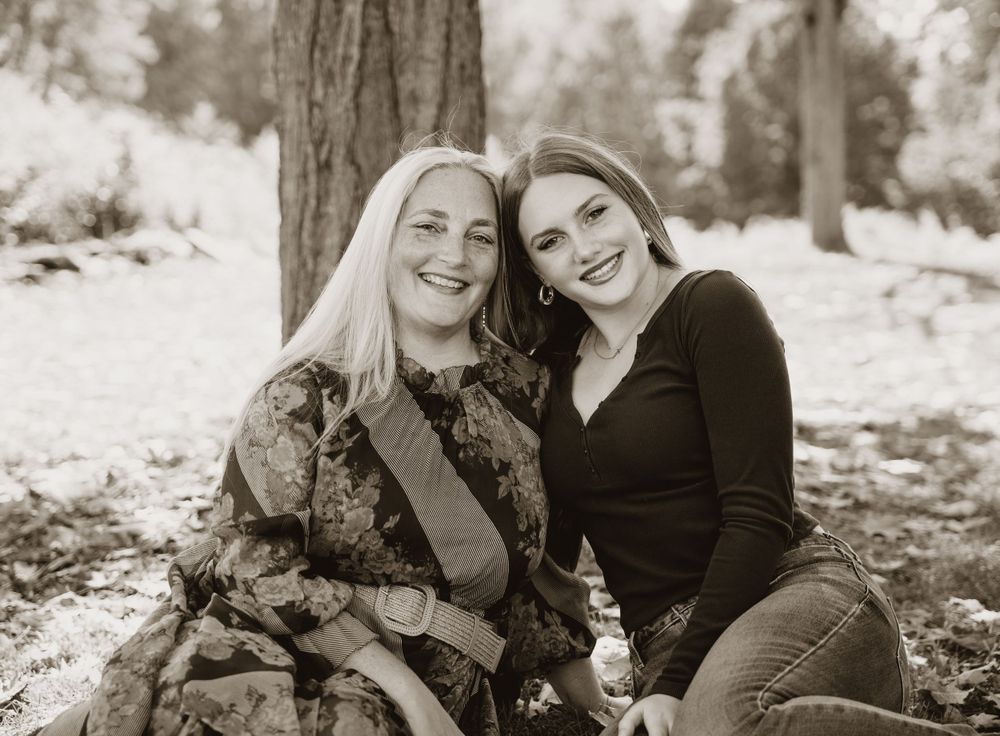 A black and white portrait of two people sitting together against a tree in a natural setting.