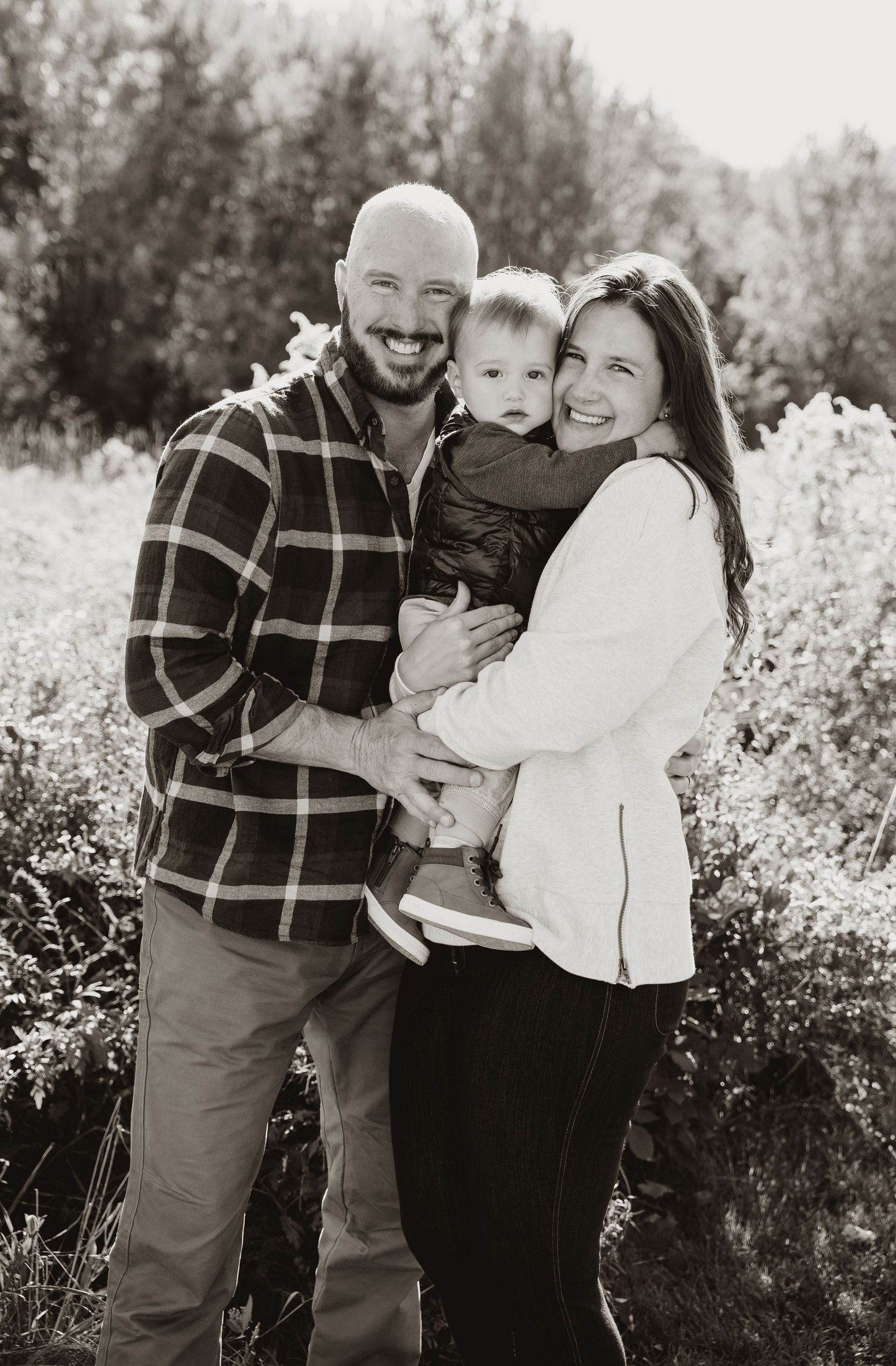 Classic black and white family portrait capturing genuine smiles in an outdoor setting.