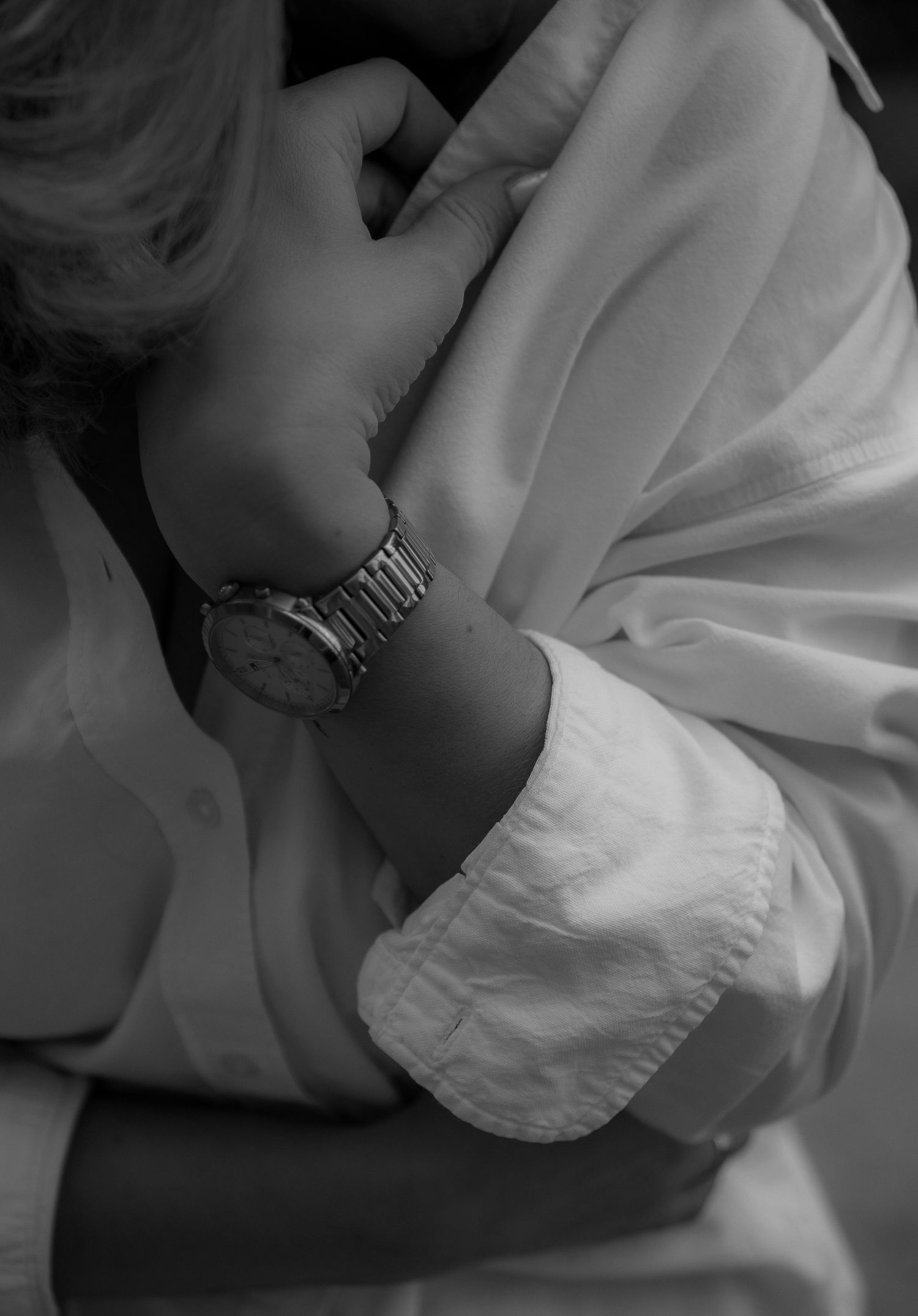 Close-up of silver watch on wrist with white sleeve in monochrome.