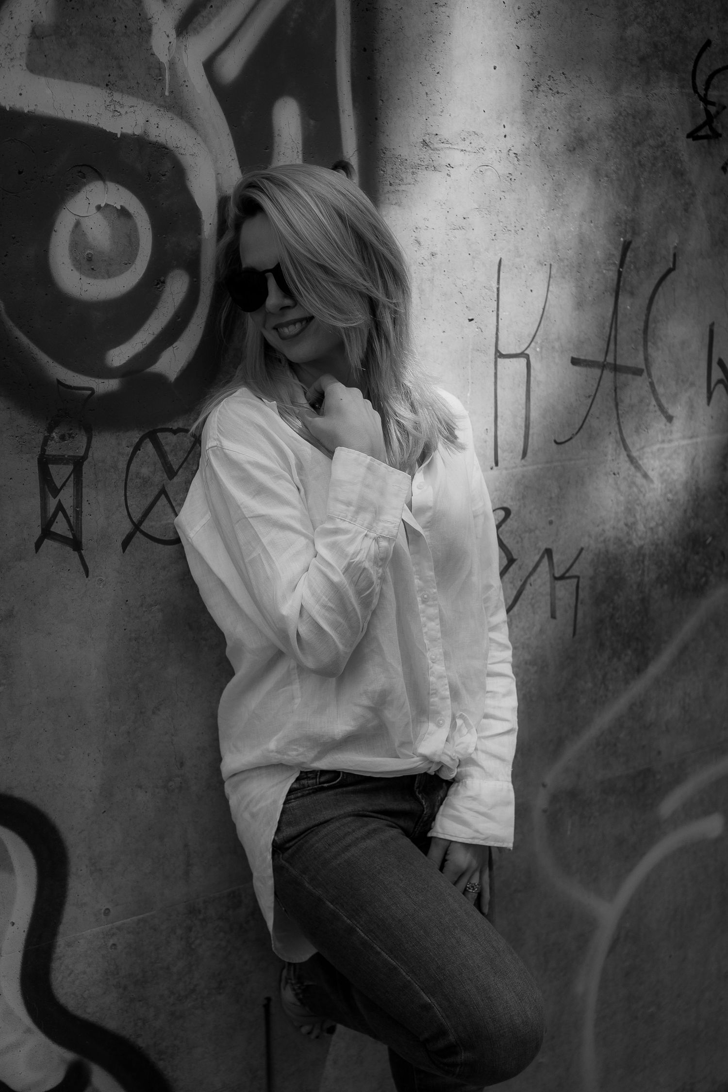 Artistic black and white portrait against graffiti wall wearing white shirt and jeans.