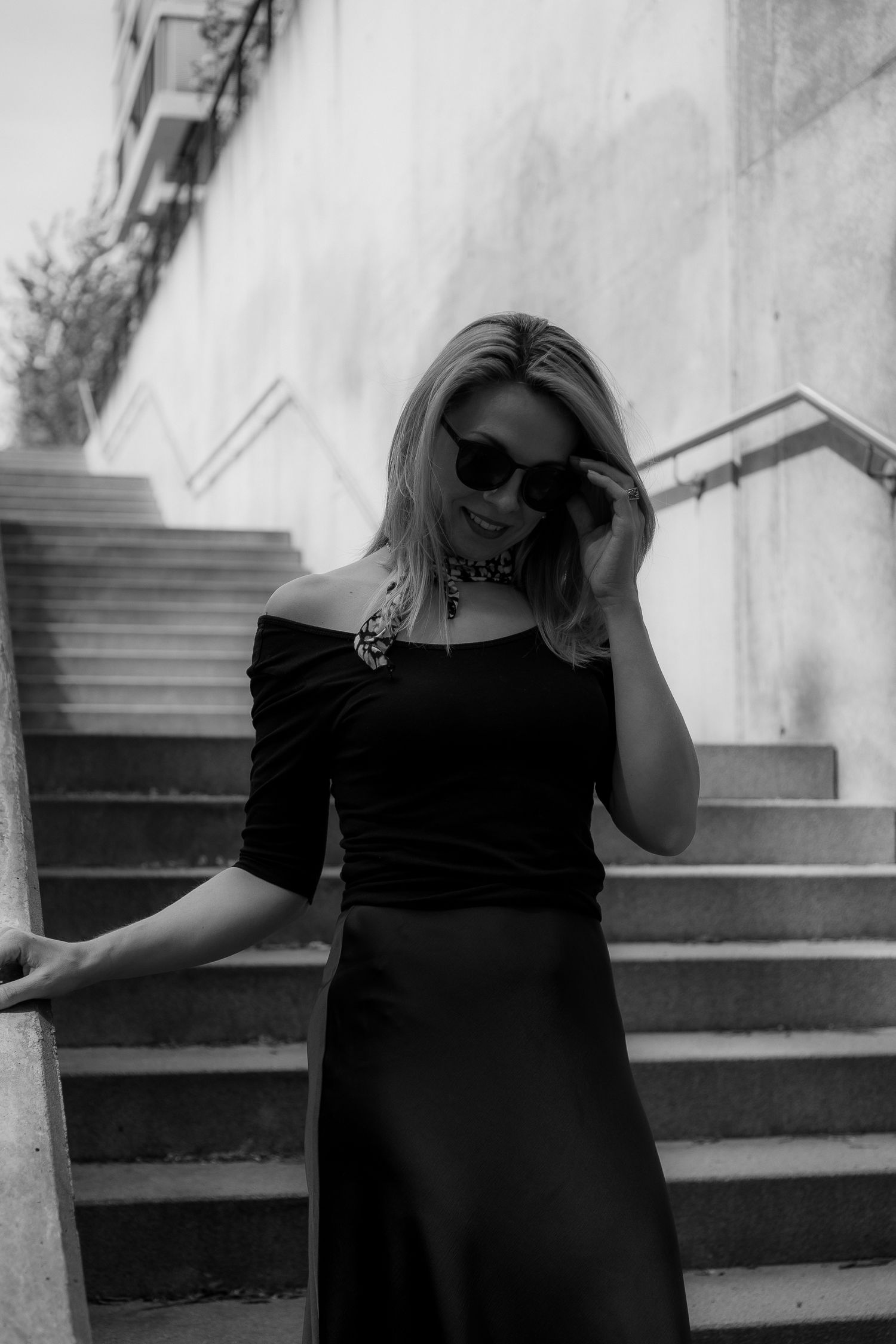 Monochrome portrait on stairs wearing black dress and sunglasses.