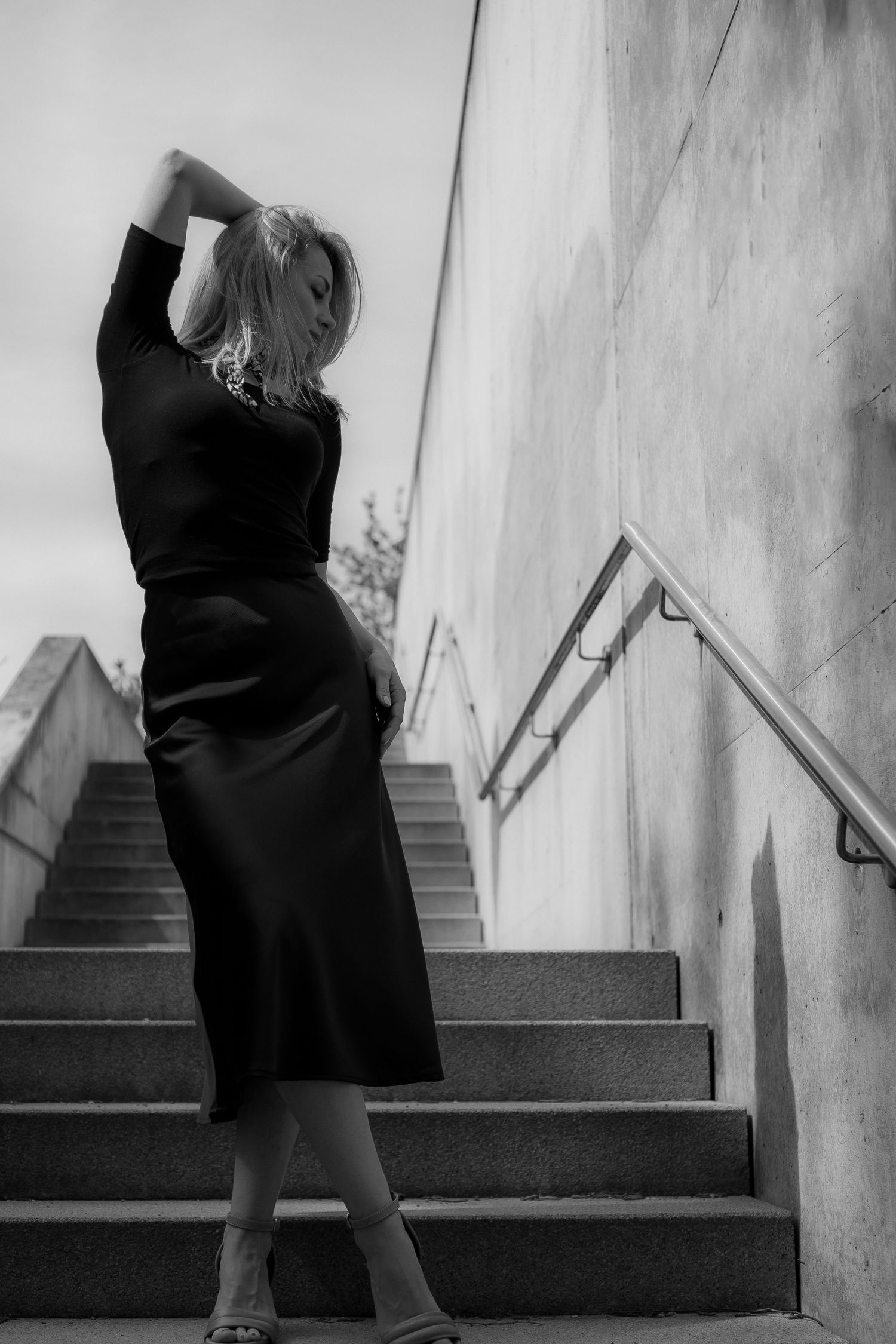 Dramatic black and white pose against wall on urban staircase.