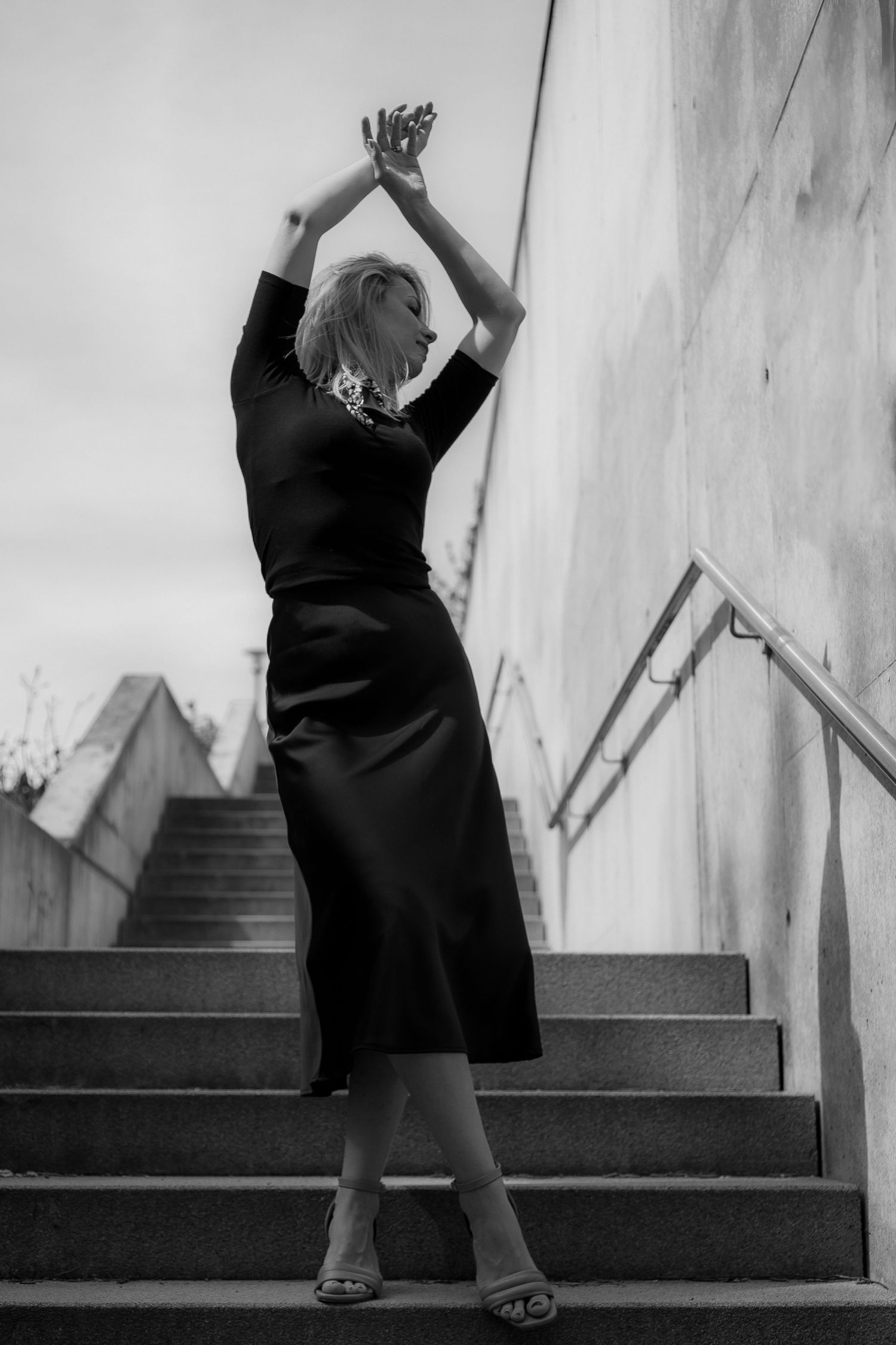 Black and white fashion pose on concrete stairs in elegant black dress.