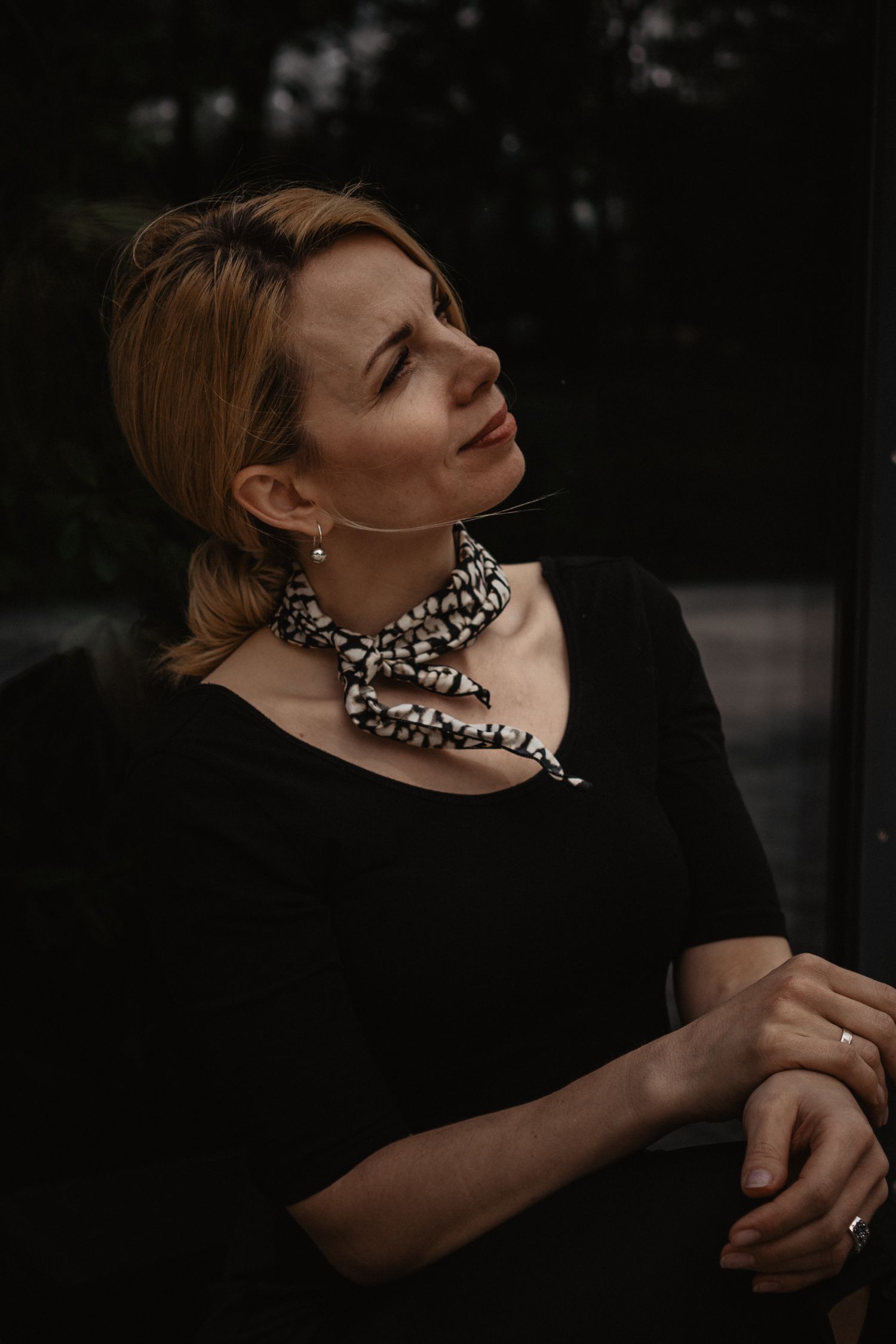 Atmospheric portrait in black featuring a statement necklace and elegant styling against a dark background.