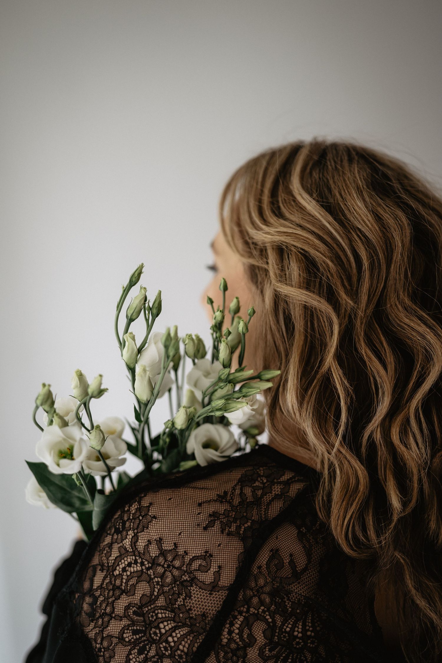Artistic portrait series featuring white flowers against black lace dress details in soft, moody lighting.