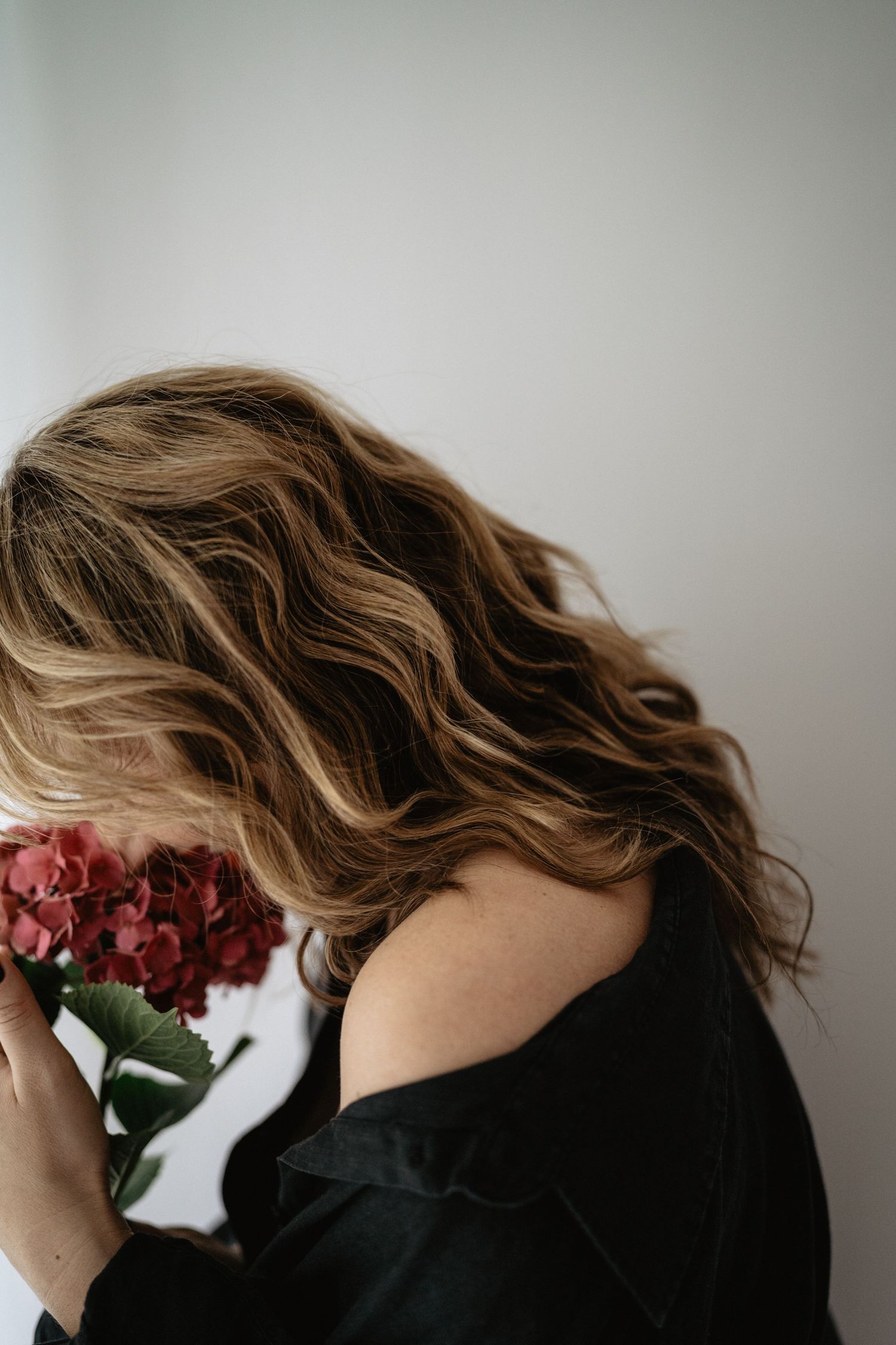 A person in black clothing poses with red roses against a light gray wall in a series of artistic portraits.