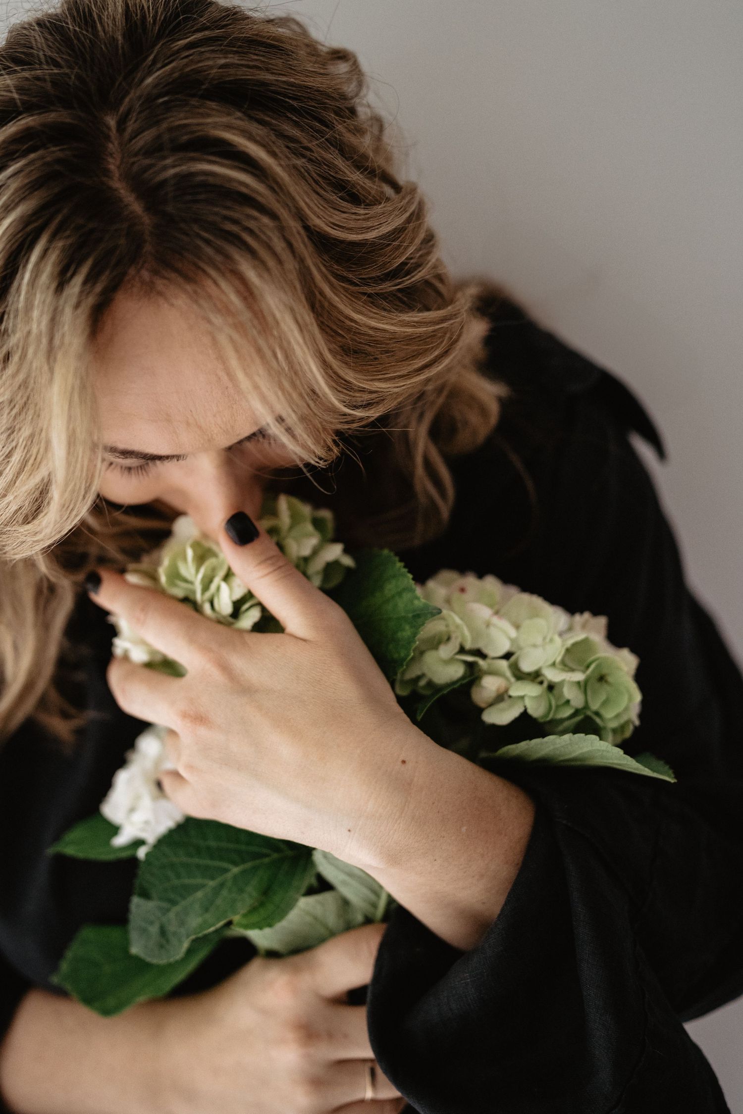 Artistic portrait of a person in black clothing holding hydrangea blooms against their face in a series of moody shots.