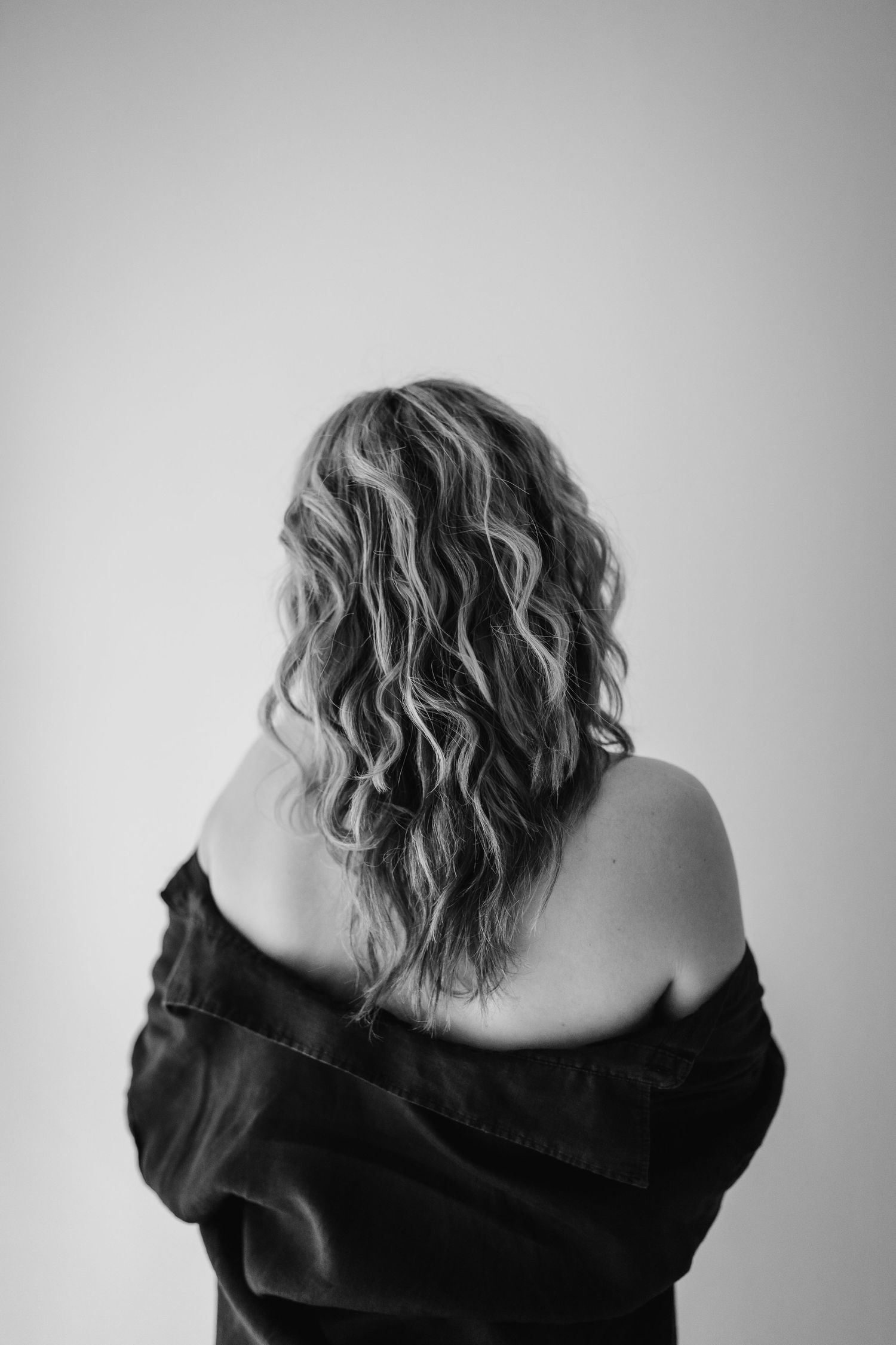 A person with tousled blonde curly hair turns their back to camera in a black top, shown in three artistic poses.