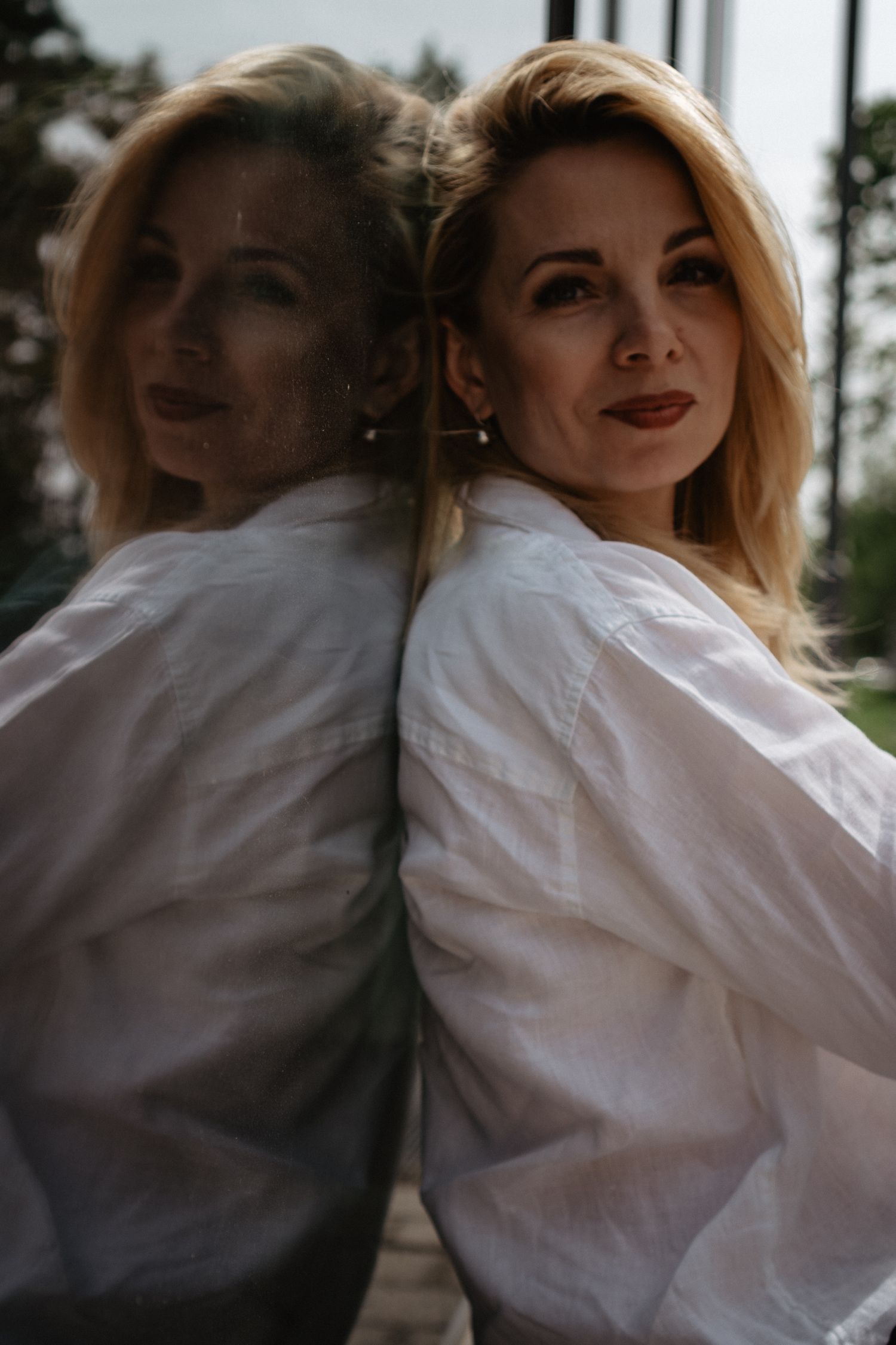 Artistic mirror reflection portrait in natural light wearing a white button-down shirt.