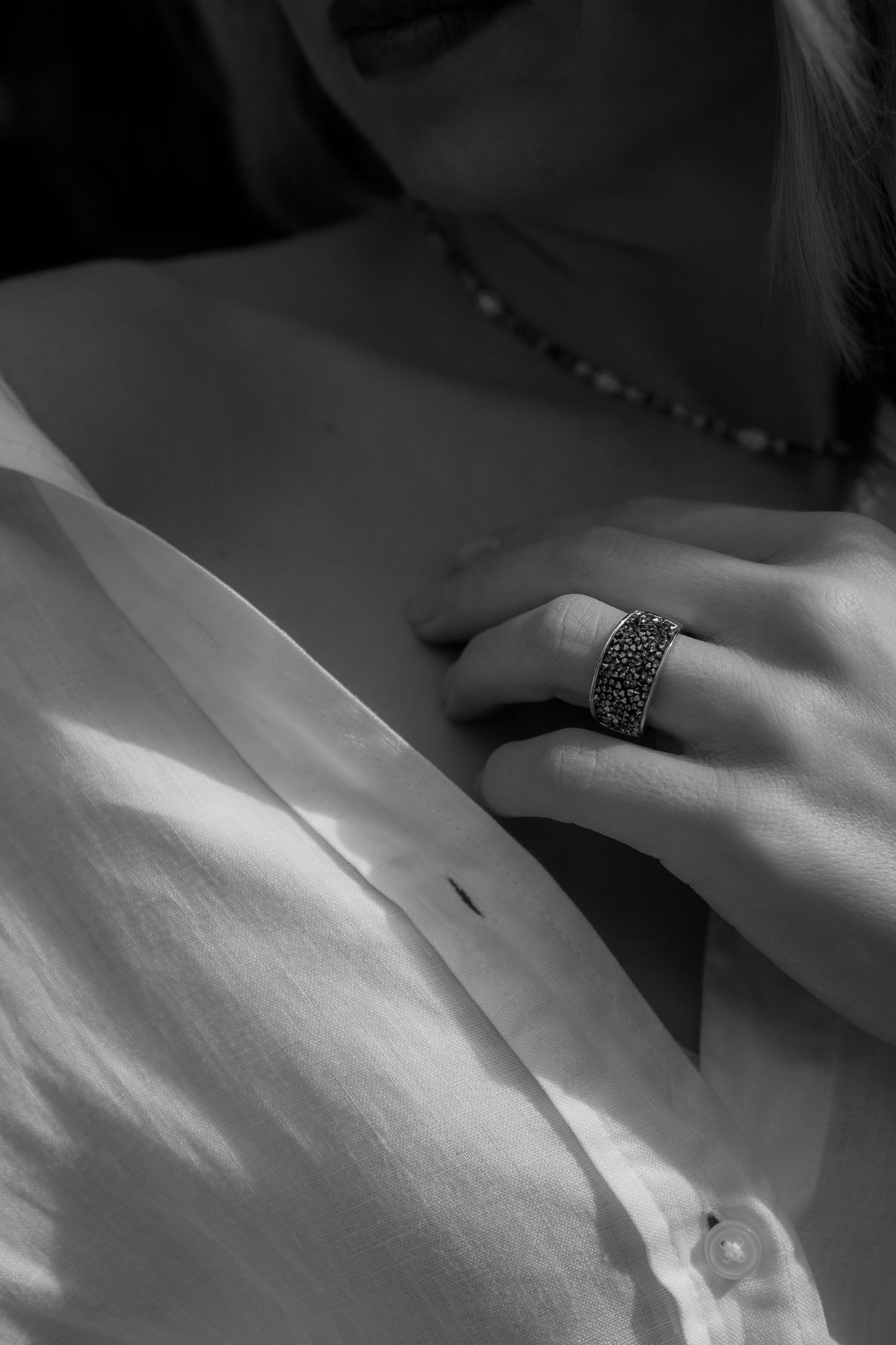 Close-up detail of an ornate ring and necklace with a white shirt in black and white.