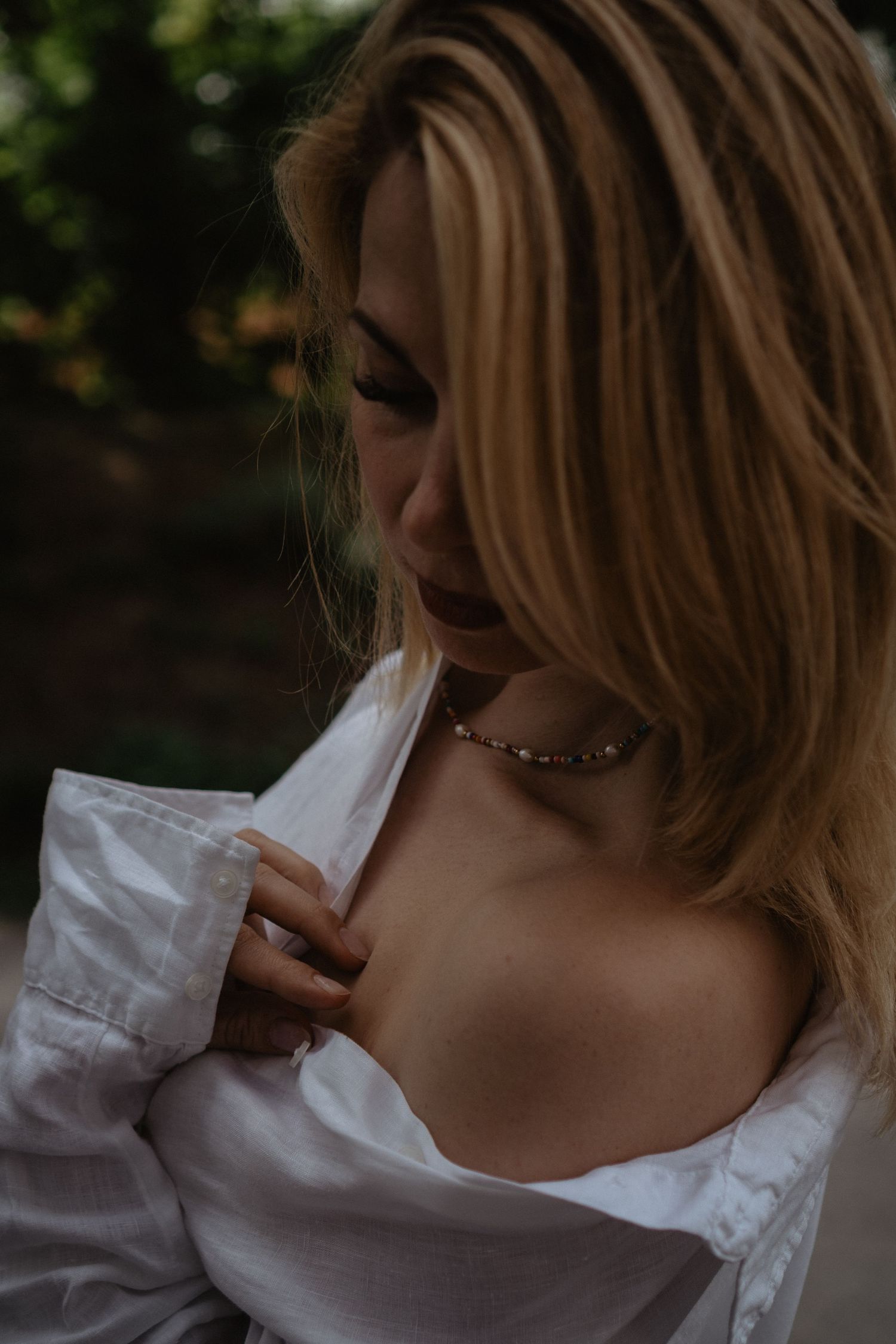Artistic portrait in natural light wearing white shirt and delicate necklace.