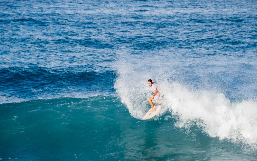 Surfer performs skillful maneuver on bright turquoise wave creating dramatic white spray.