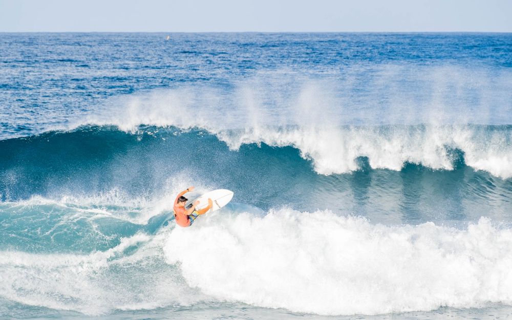 A surfer carves along the face of a large breaking wave in crystal blue ocean waters.