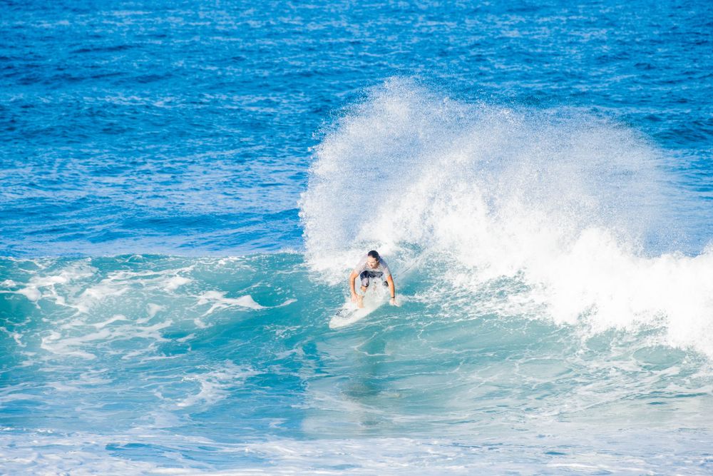 A surfer rides through the spray on a perfectly formed blue wave in tropical waters.