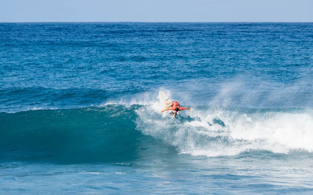 Surfer riding and cutting through a large turquoise ocean wave with white spray in vibrant tropical waters.