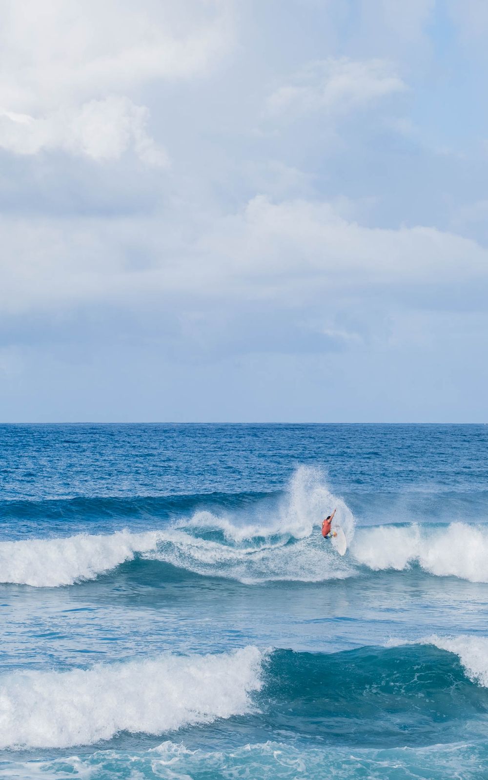 Dynamic surfing action shot showing rider launching off a breaking ocean wave against cloudy sky.