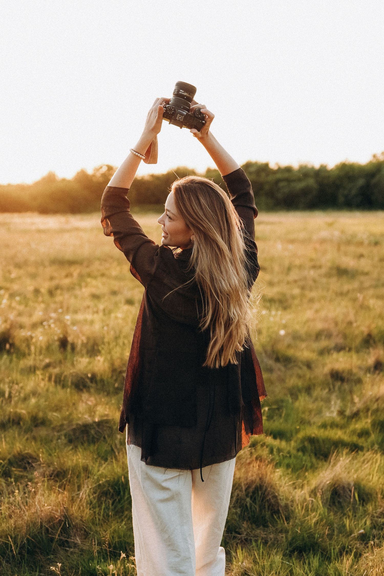 Person holding up camera while dancing in field at golden hour.