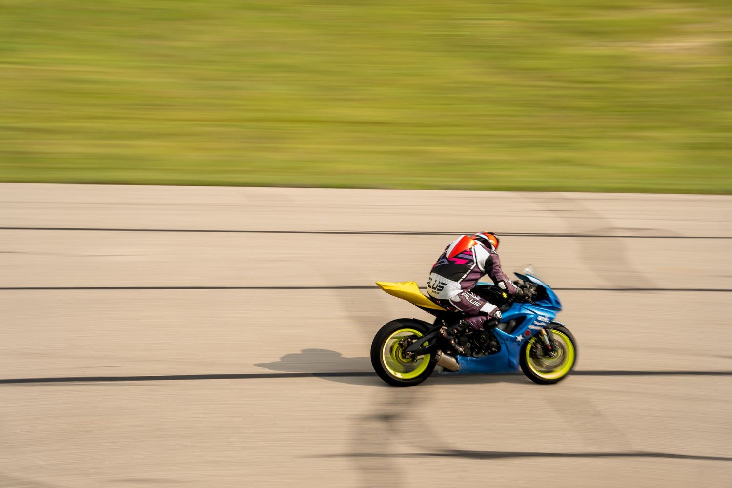 Blue and yellow racing motorcycle speeding on track with motion-blurred green grass.