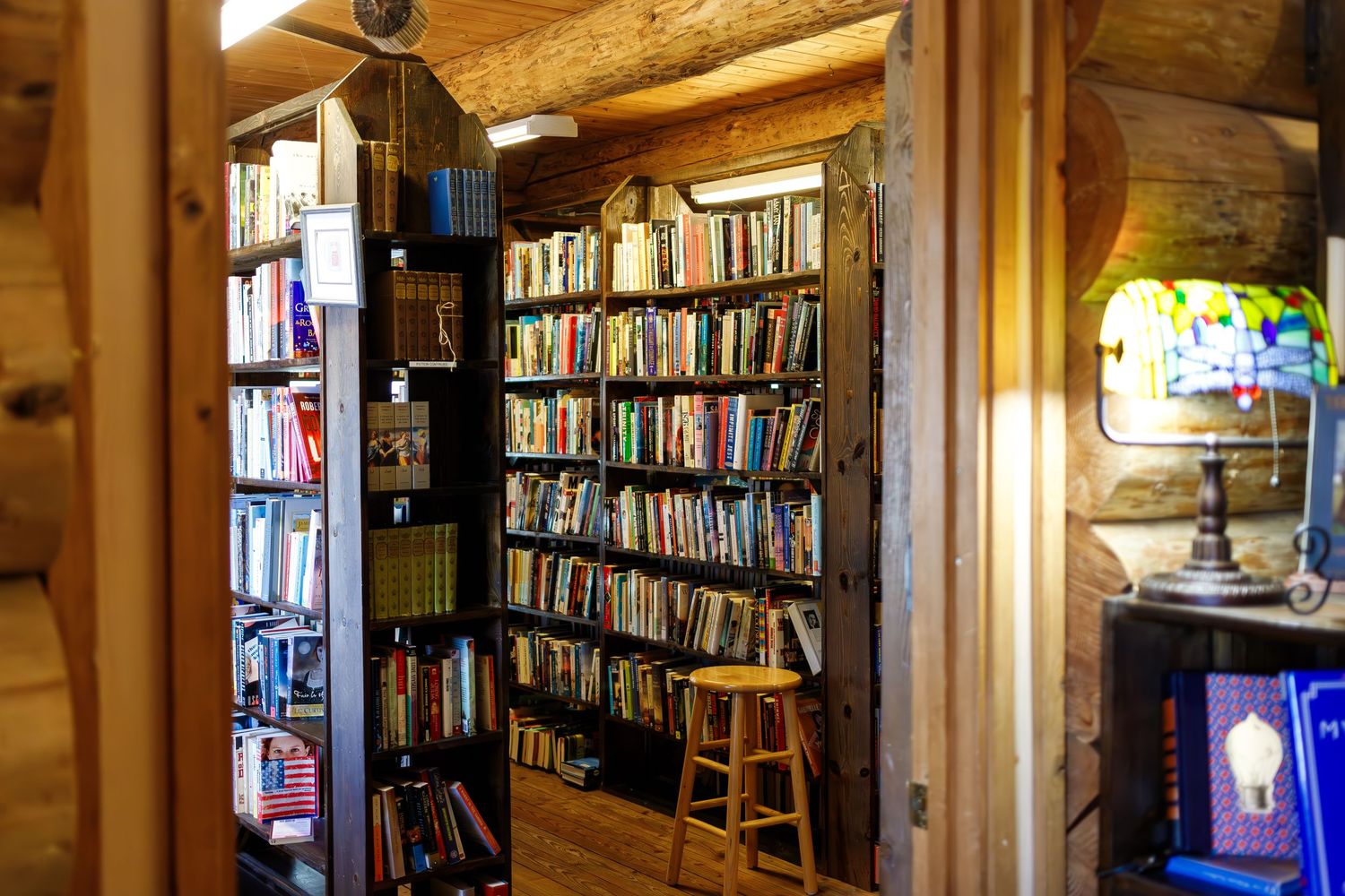 Warm interior lighting illuminates floor-to-ceiling bookshelves in log cabin bookstore.