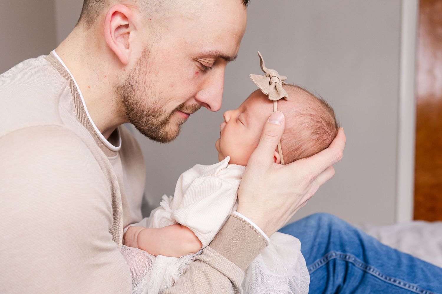 A tender moment between an adult in a beige sweater and a newborn baby touching foreheads together.